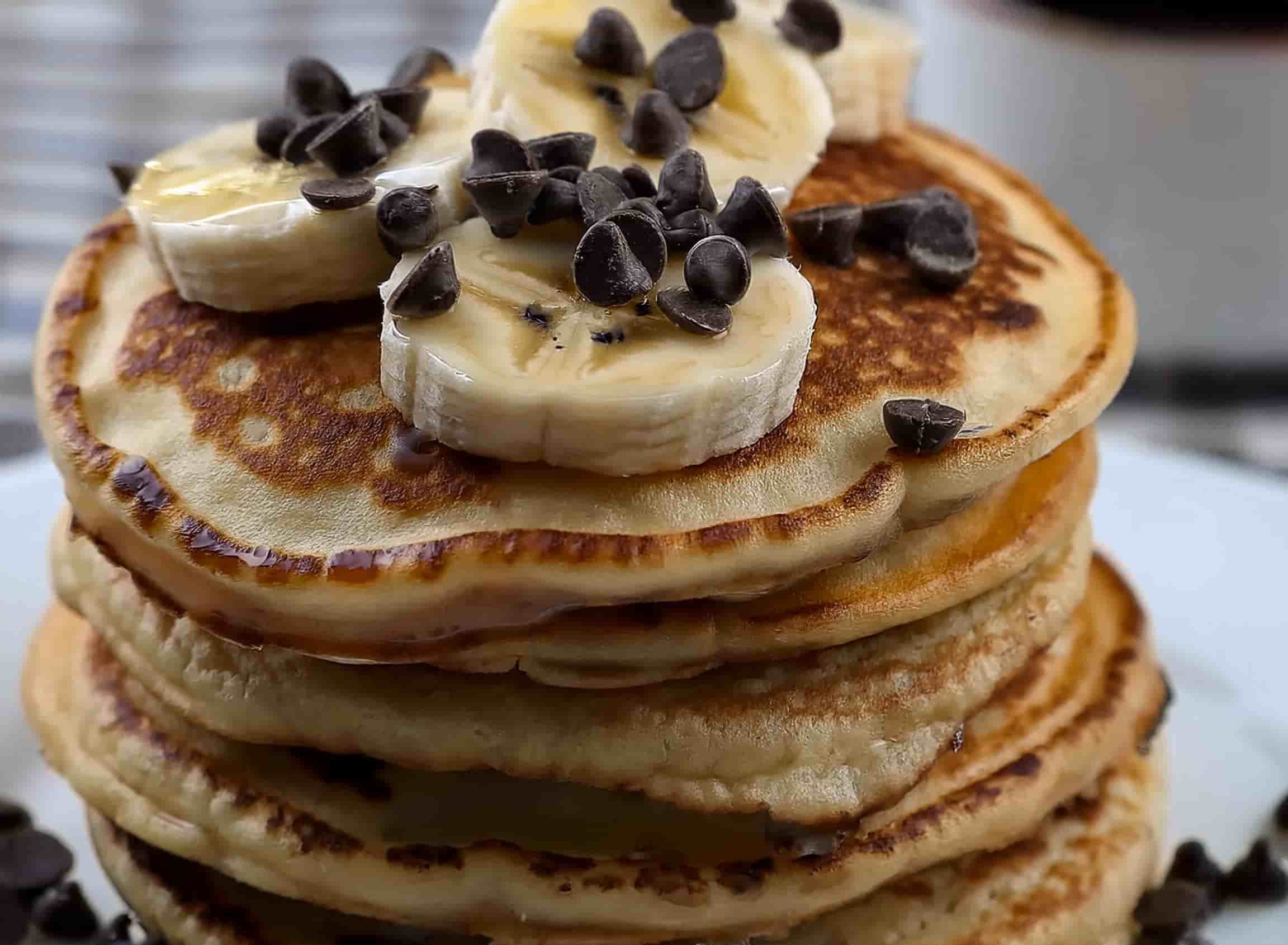 Stack of warm banana chocolate chip pancakes topped with sliced bananas and a drizzle of syrup.
