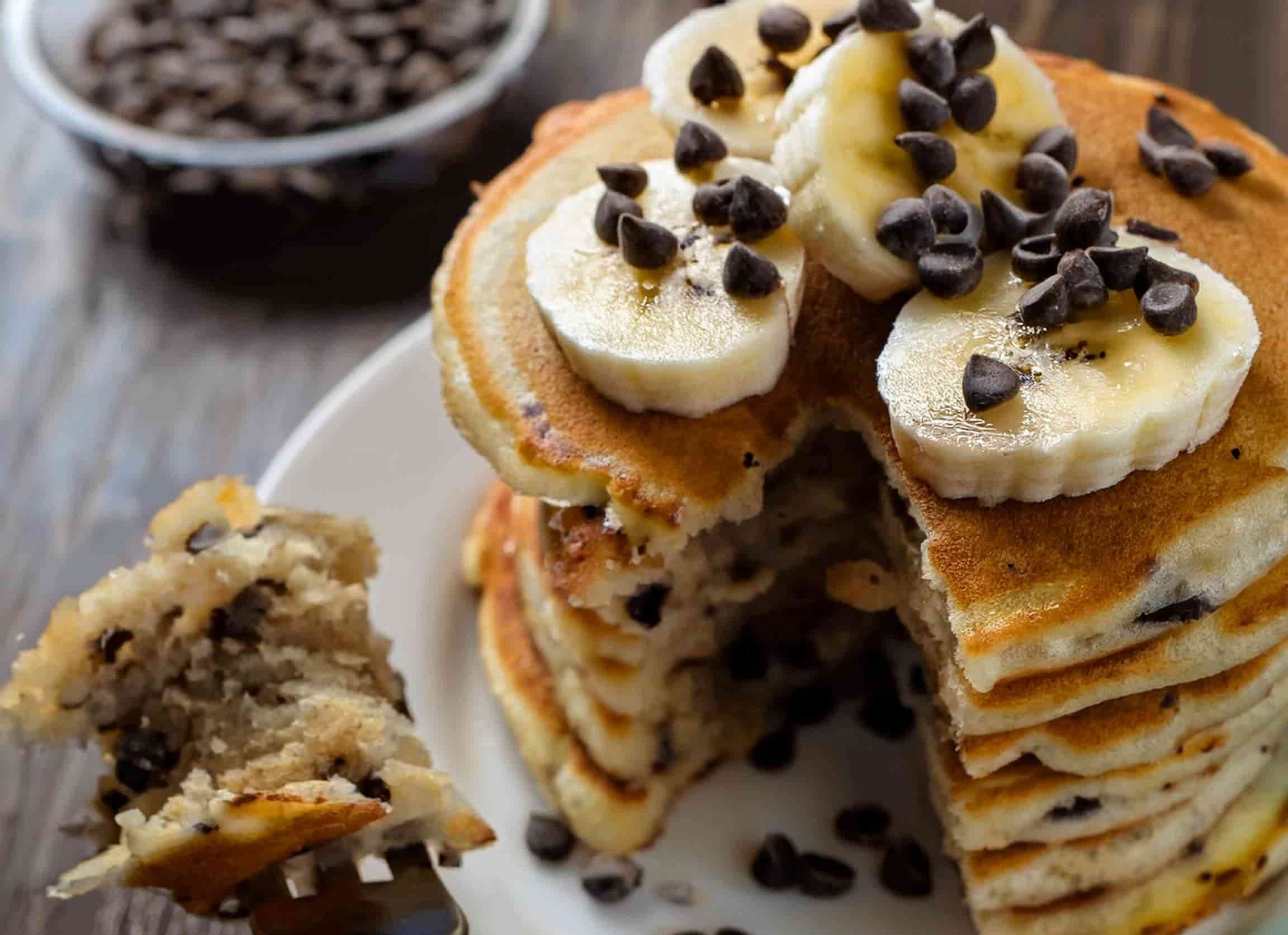 Delicious banana chocolate chip pancakes sliced and served on a plate with a fork beside them.